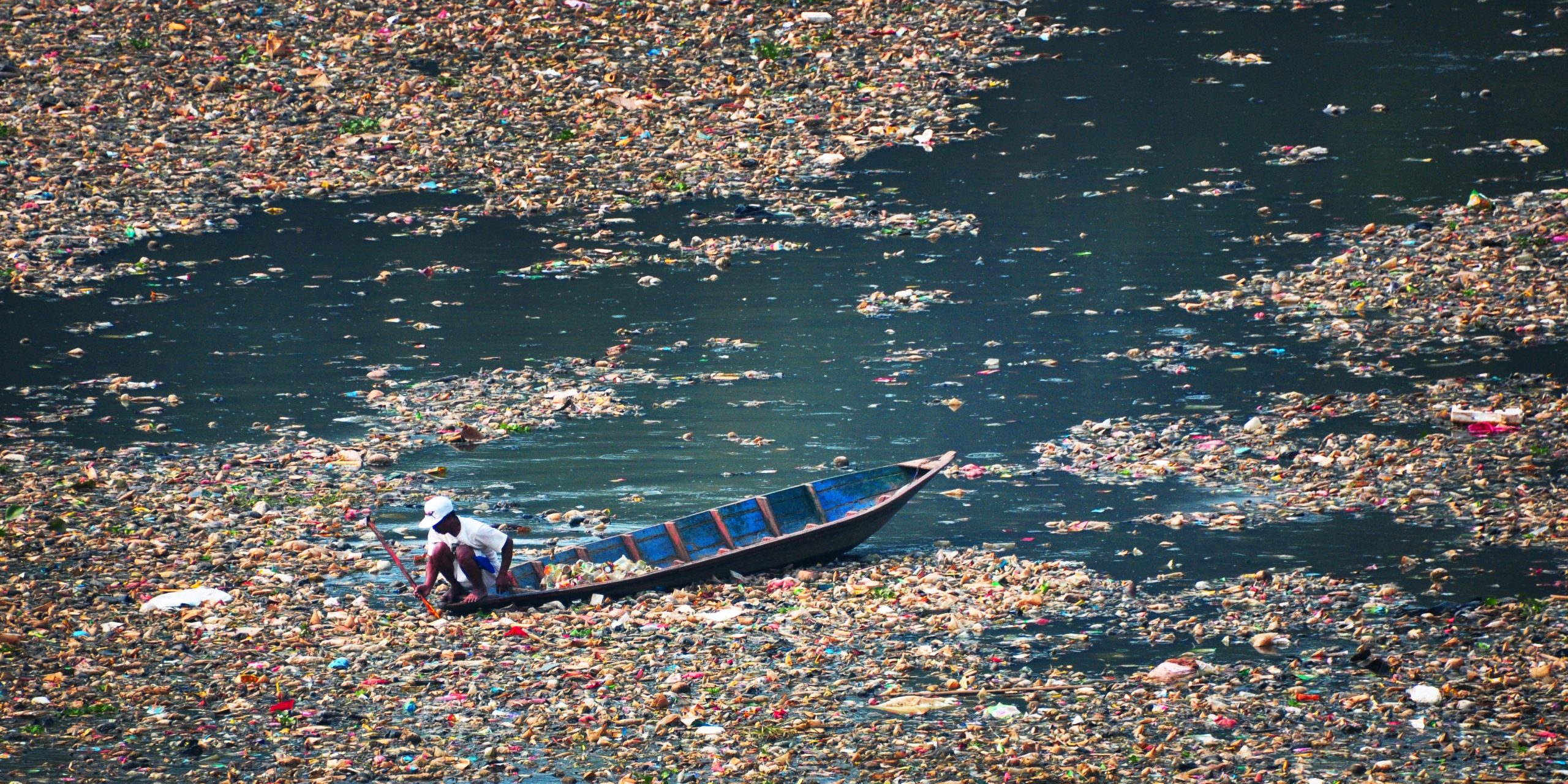 Un hombre busca entre la basura en el río