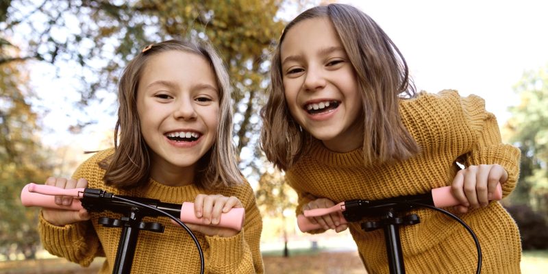 Gemelas sonriendo y montando scooters