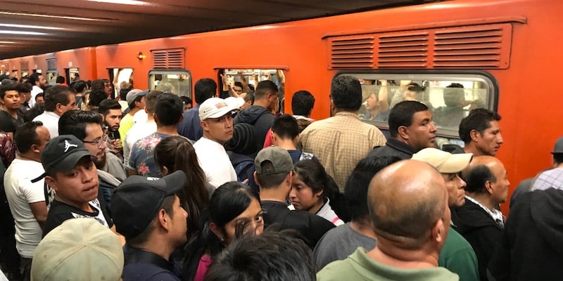 Una multitud de personas intenta entrar a un tren, en una ciudad superpoblada.