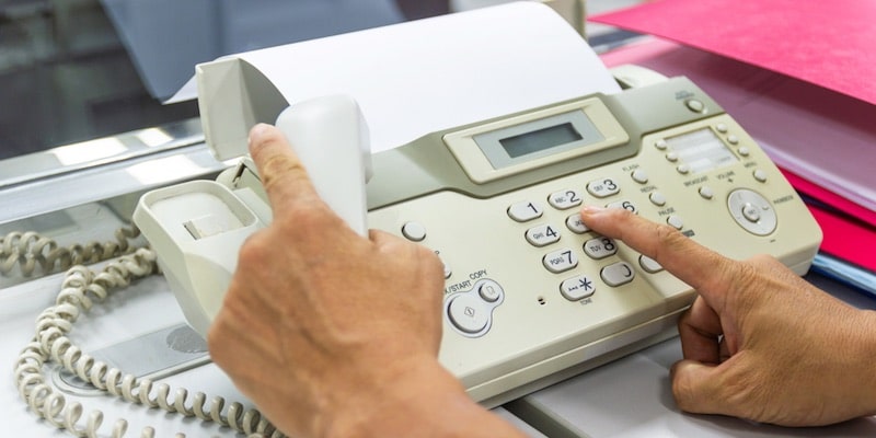 Una persona marca un número en una máquina de fax para poder enviar un documento.