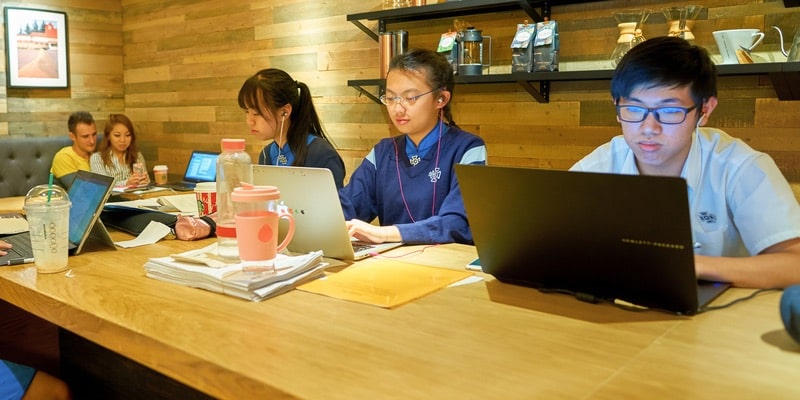 Un grupo de jóvenes de la generación z trabaja en un café frente a sus computadoras.
