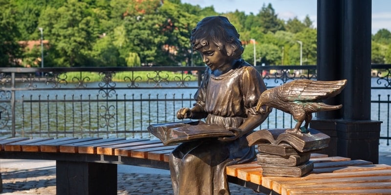 En un parque hay una escultura de una niña leyendo junto a un pájaro.
