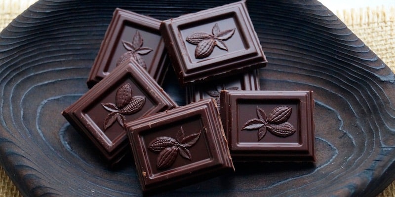 Sobre un plato de madera hay chocolate con un dibujo de la planta de cacao.