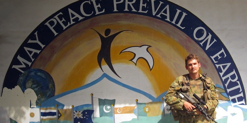 Un soldado se encuentra frente a un mural que aboga por la paz.