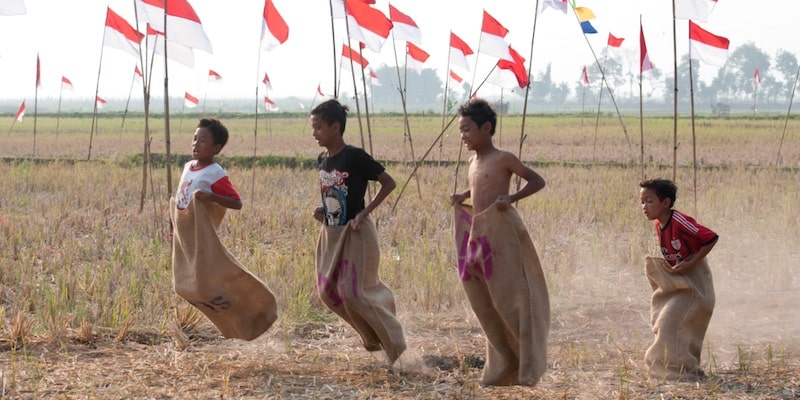 Cuatro niños compiten saltando usando sacos de arpillera.