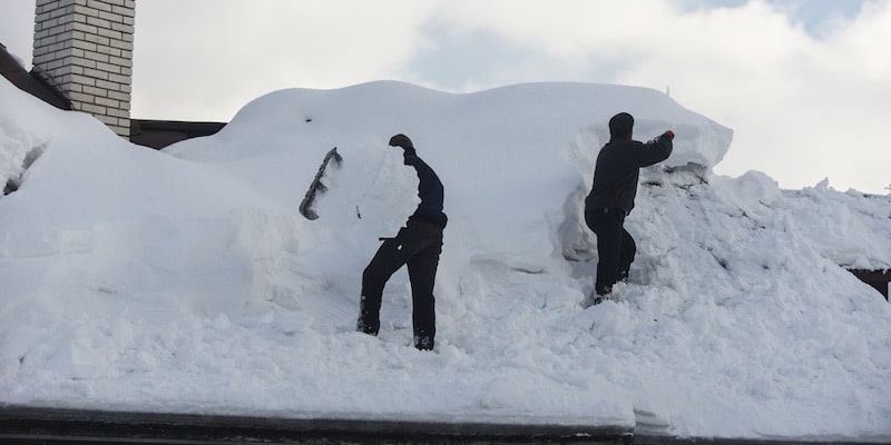 Dos hombres industriosos trabajan para sacar nieve de un techo.