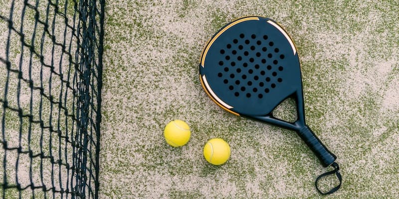 Una raqueta de pádel y dos pelotas se encuentran junto a la red.