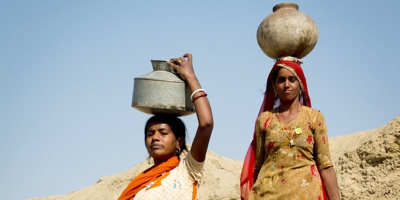 Dos mujeres perseverantes transportan agua.