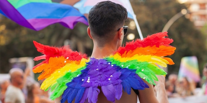 Una joven queer lleva alas de muchos colores en un desfile del orgullo gay.