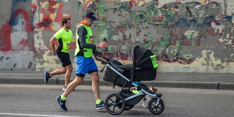 Un hombre corre una maratón llevando el carrito de su hijo.