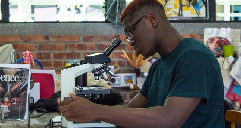 Un estudiante con anteojos utiliza un microscopio en el aula.