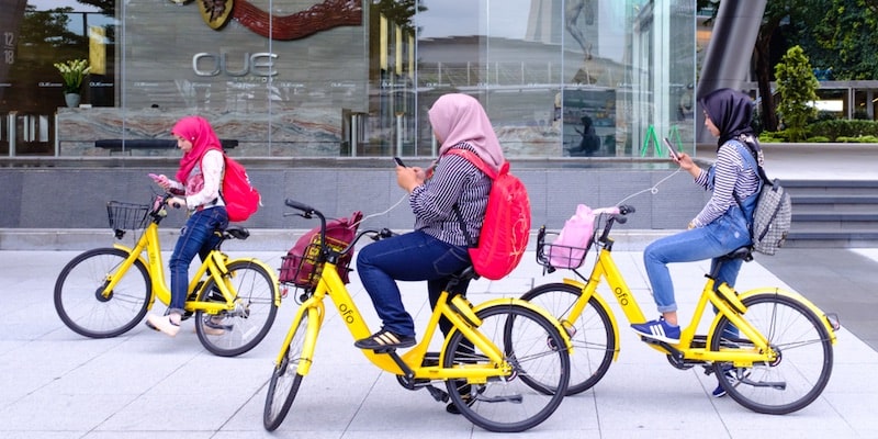 Tres niñas utilizan objetos tecnológicos como bicicletas y teléfonos mientras pasean.