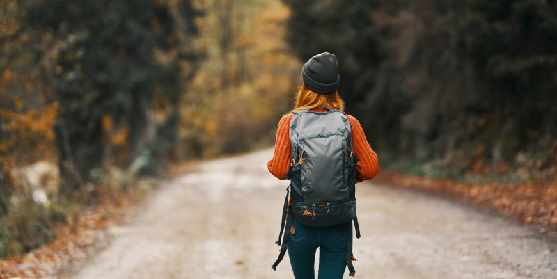 Mujer de espaldas mirando hacia un camino entre árboles.