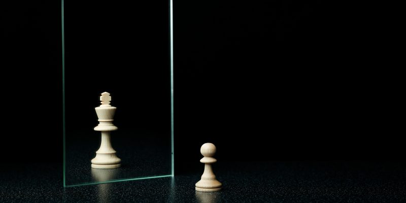 Piezas de peón y rey de ajedréz frente a un espejo.